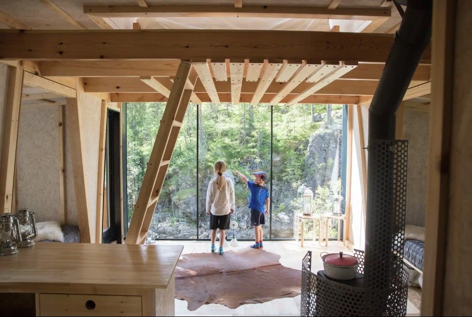 Two children standing inside a treetop cabin and looking out the window