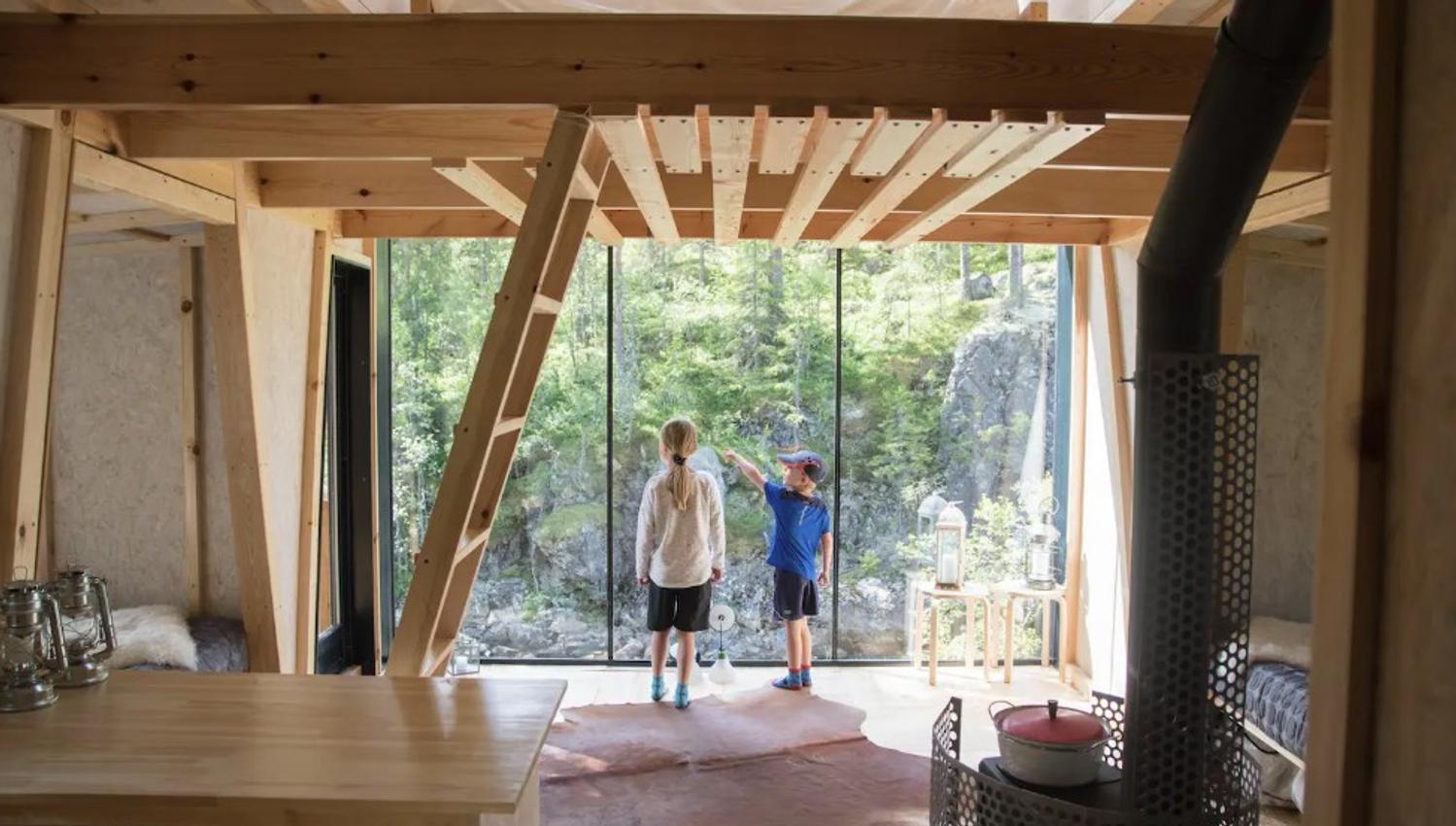 Two children standing inside a treetop cabin and looking out the window
