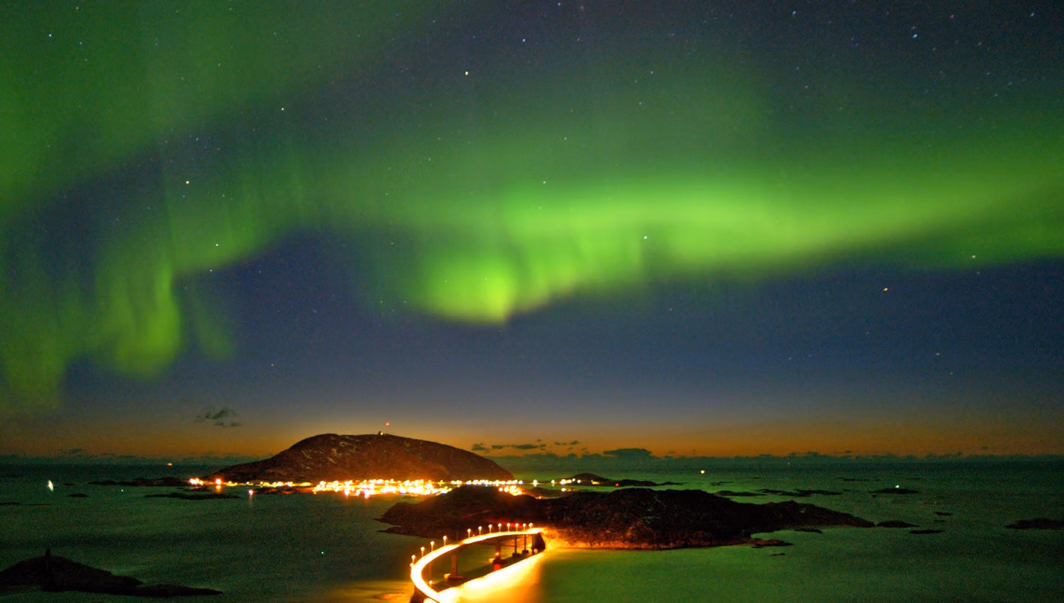 Grønnskimrende nordlys over himmelen, med en opplyst vei som strekker seg over mørkt vann