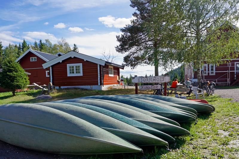 Canoes laying upside down on a lawn in front of small red houses.