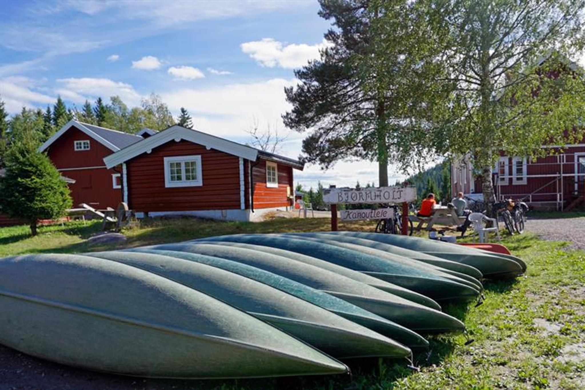Canoes laying upside down on a lawn in front of small red houses.