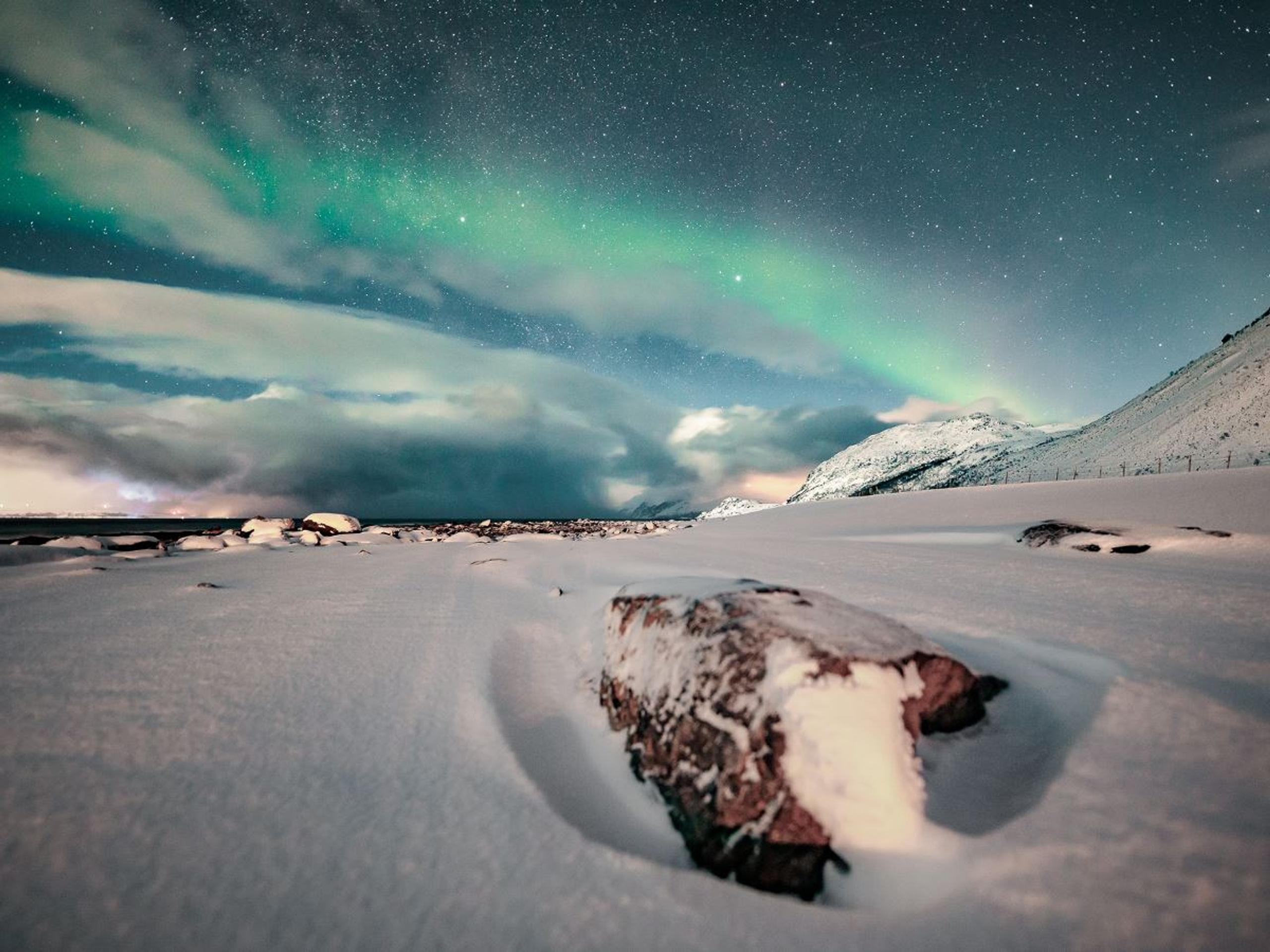 Northern lights dancing across the sky, snow coverd coast in the foreground