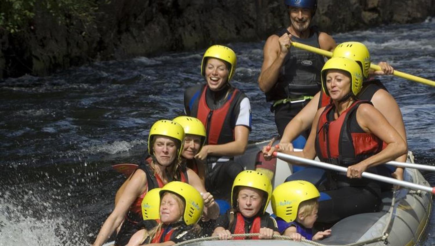 Rafting mit Menschen in schwarzen Neoprenanzügen und roten Schwimmwesten + gelben Helmen.