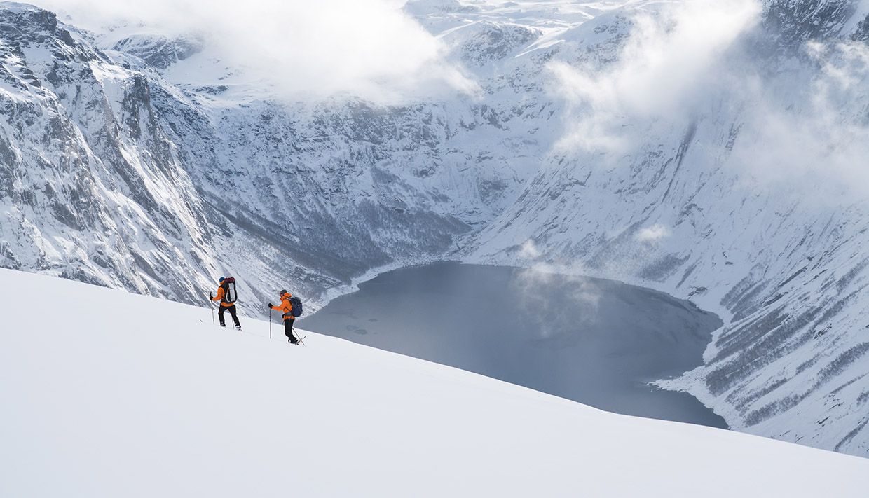 Two snowshoe hikers traversing steep winter terrain overlooking the fjord near Trolltunga.
