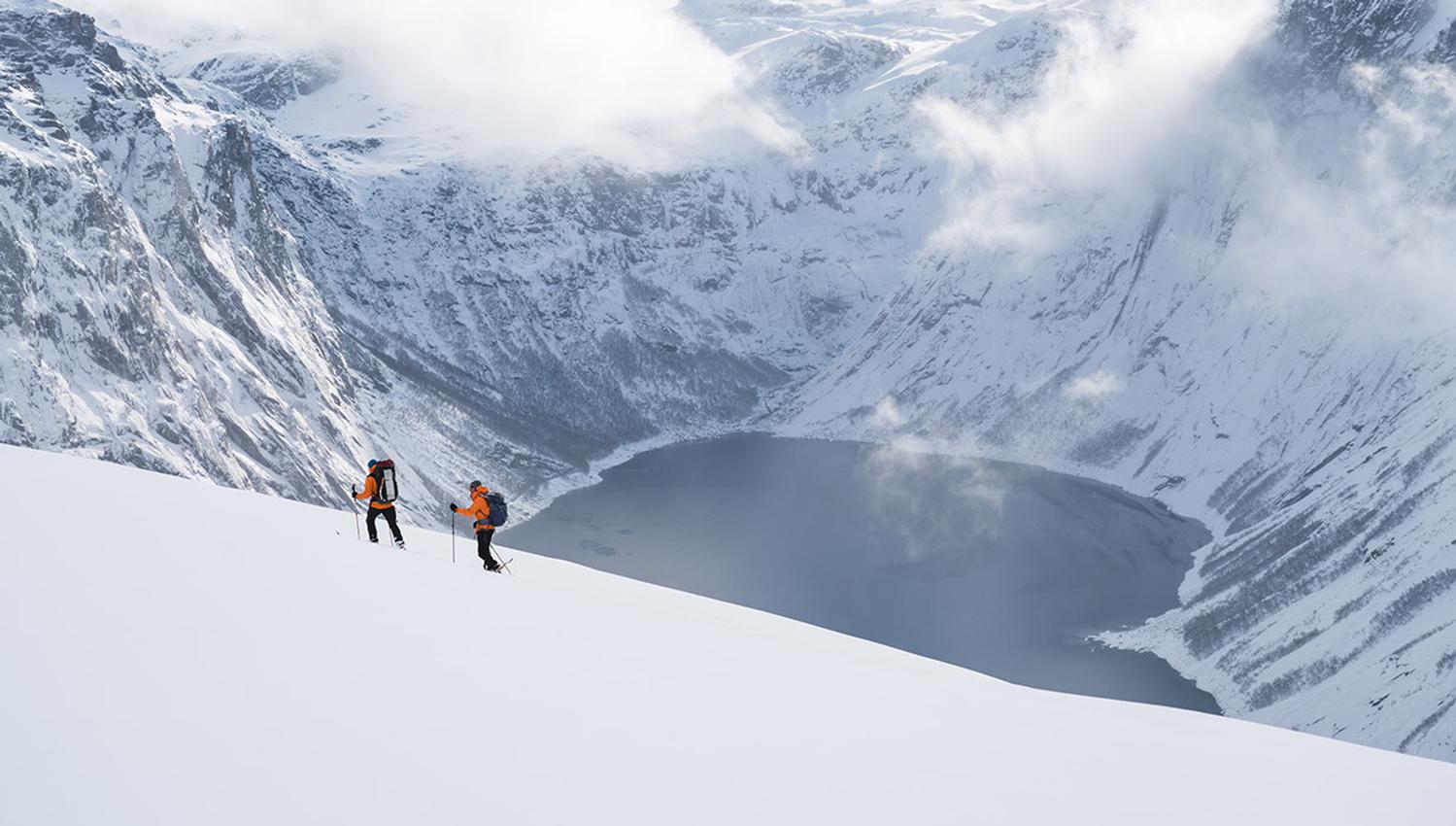 Two snowshoe hikers traversing steep winter terrain overlooking the fjord near Trolltunga.