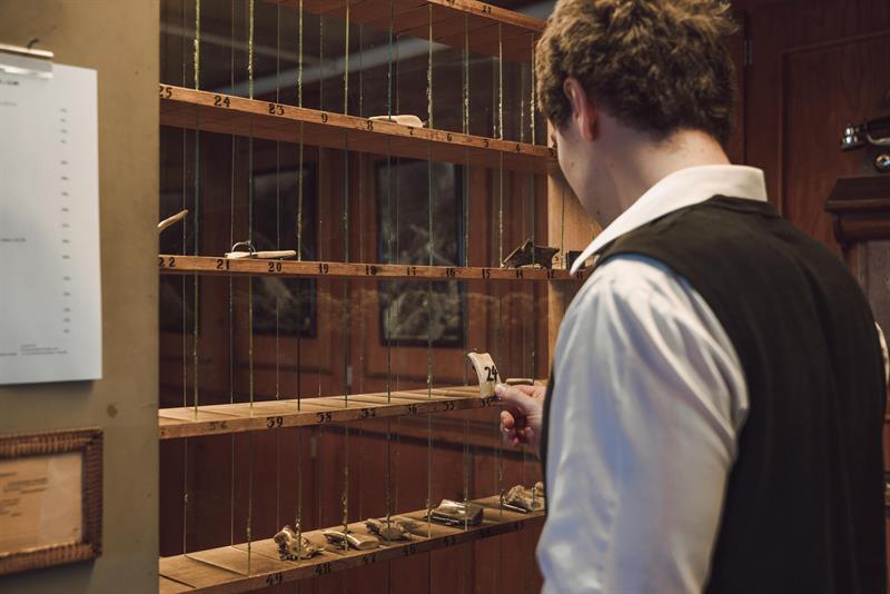 A receptionist is picking an old fashion room key from the key cabinet.