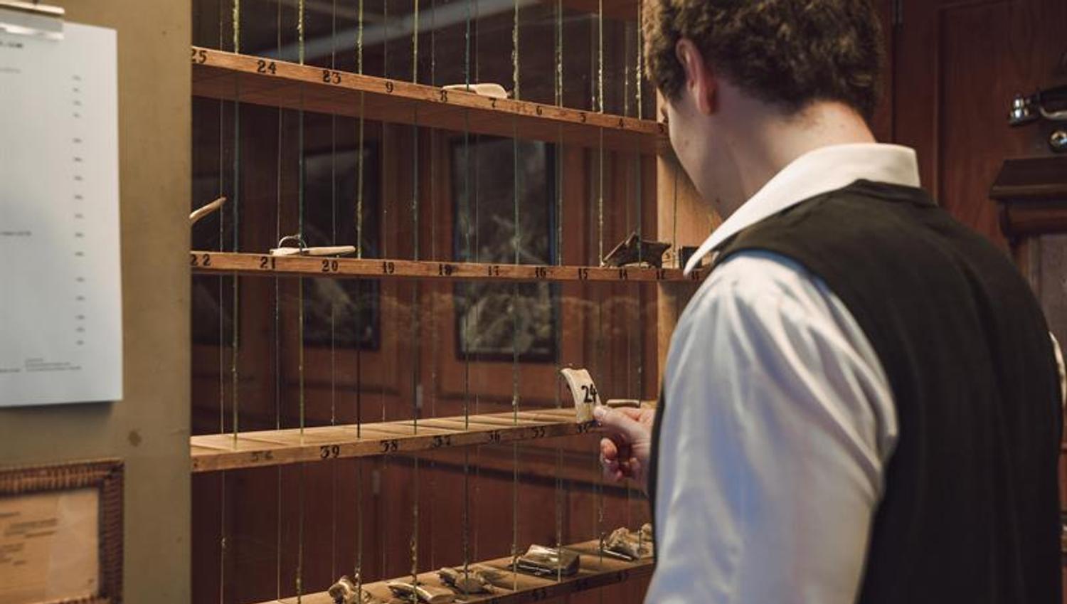 A receptionist is picking an old fashion room key from the key cabinet.