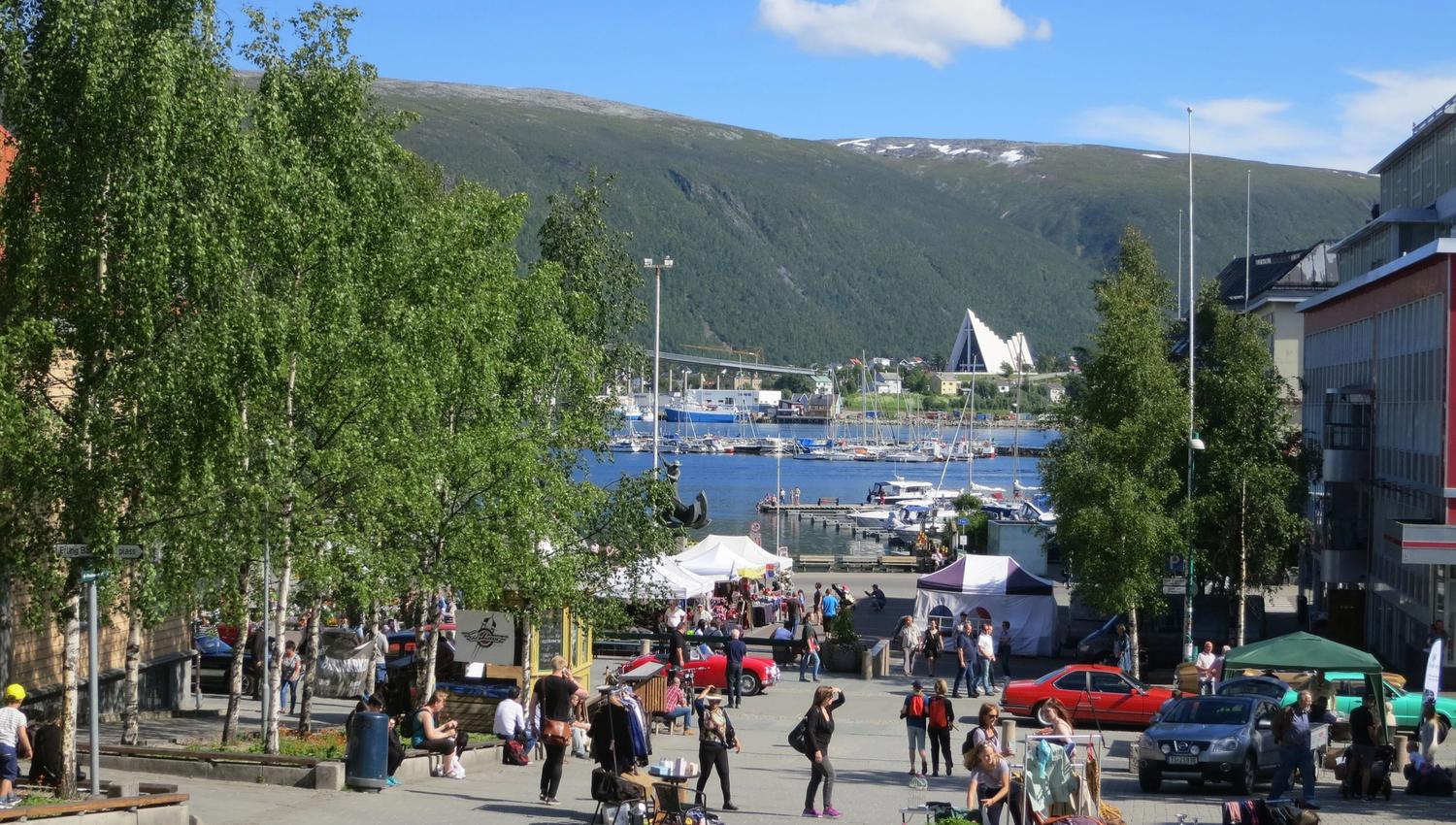 Lively town square with stalls, benches, and a view of the harbour and mountains in the background.