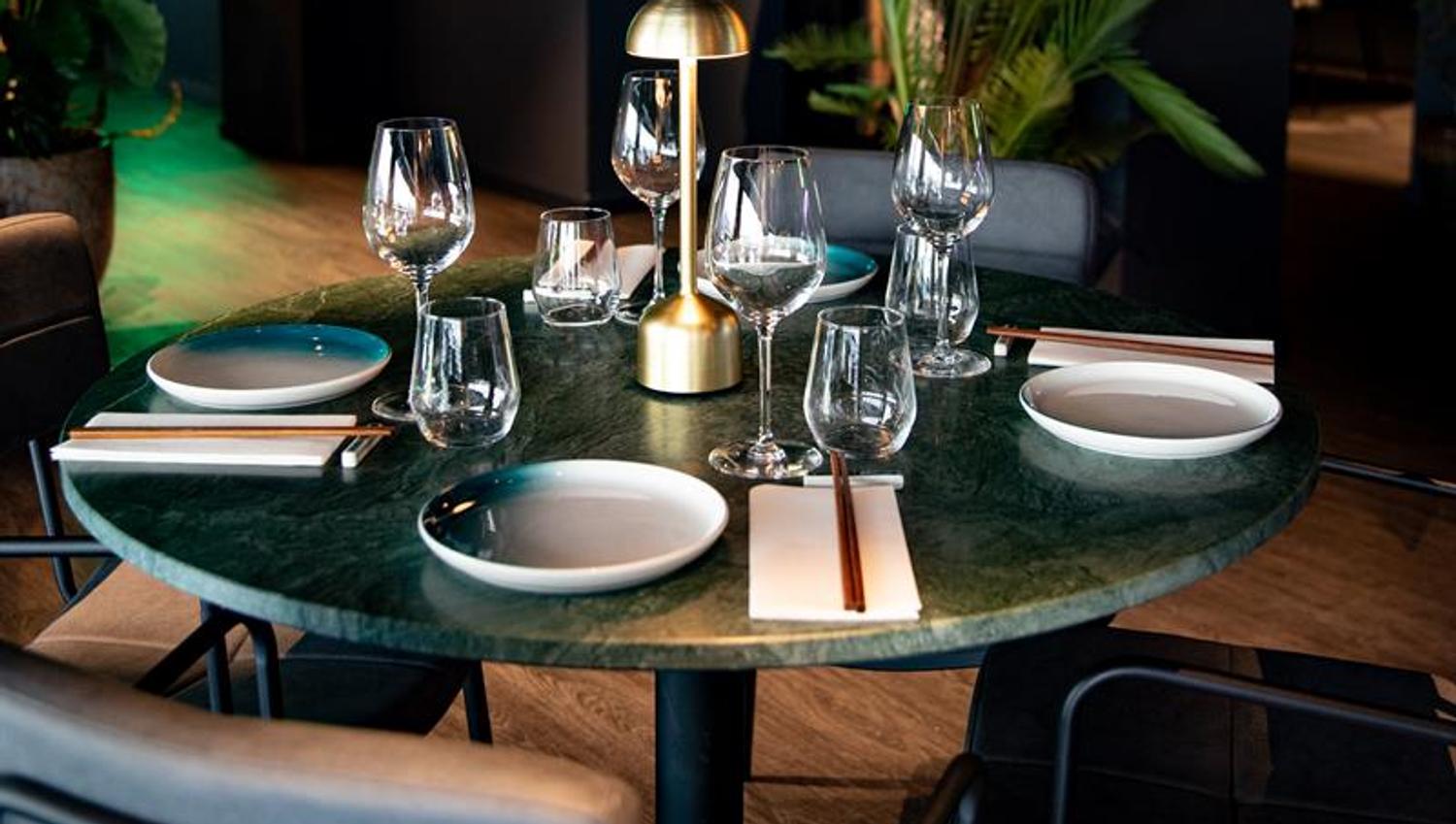 Round dining table with gold lamp, plates, glasses and crockery on