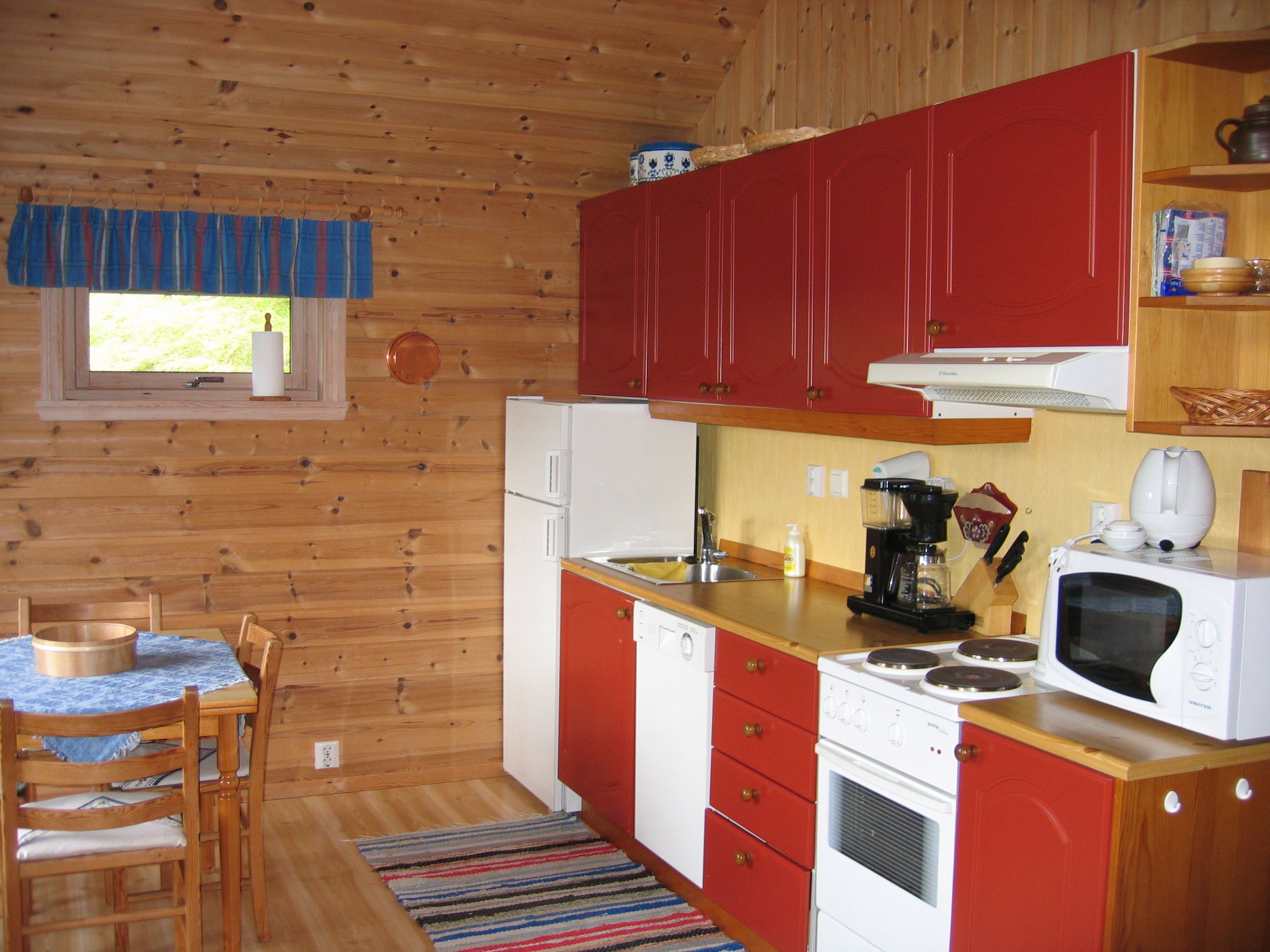 Cozy Norwegian cabin kitchen with red cabinets, wooden paneling, and full amenities.