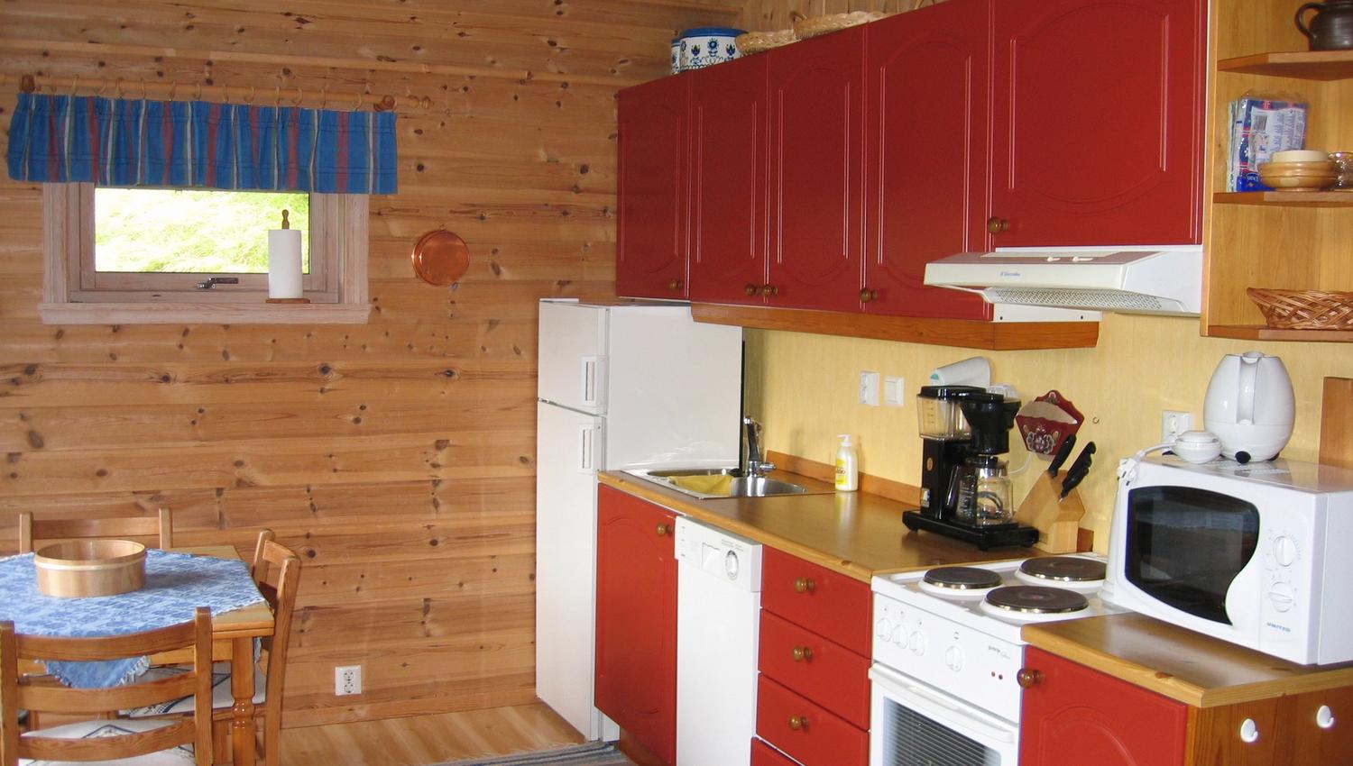 Cozy Norwegian cabin kitchen with red cabinets, wooden paneling, and full amenities.