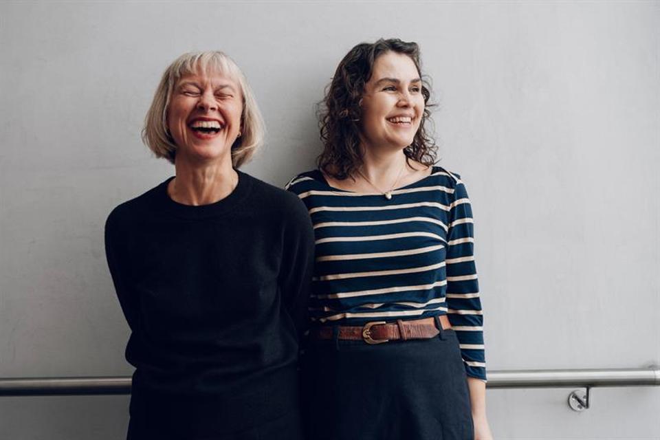 Two women smiling with a grey wall in the background