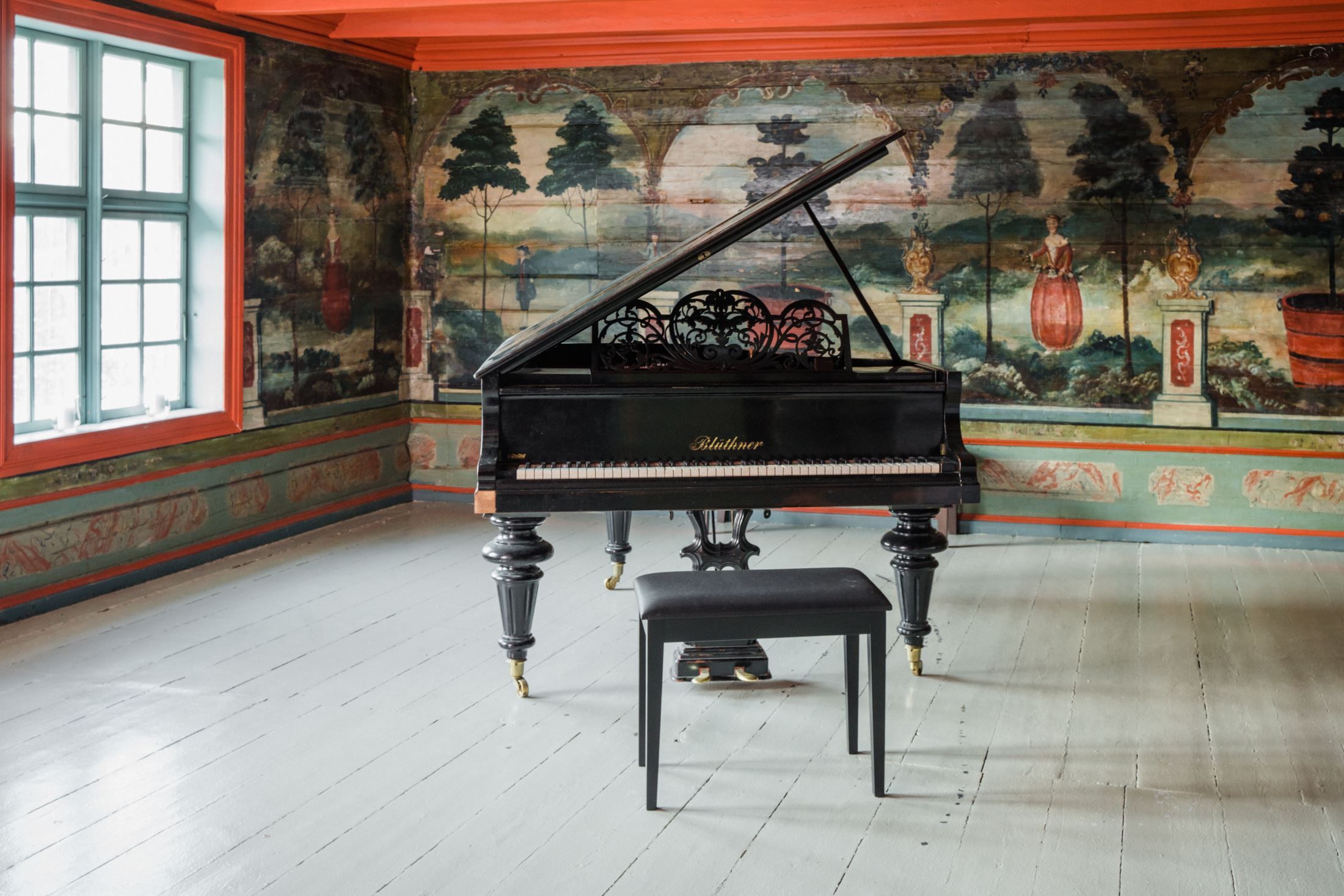 The Red Hall at Skrivergaarden, featuring a grand piano and decorative paintings on the original timber walls.