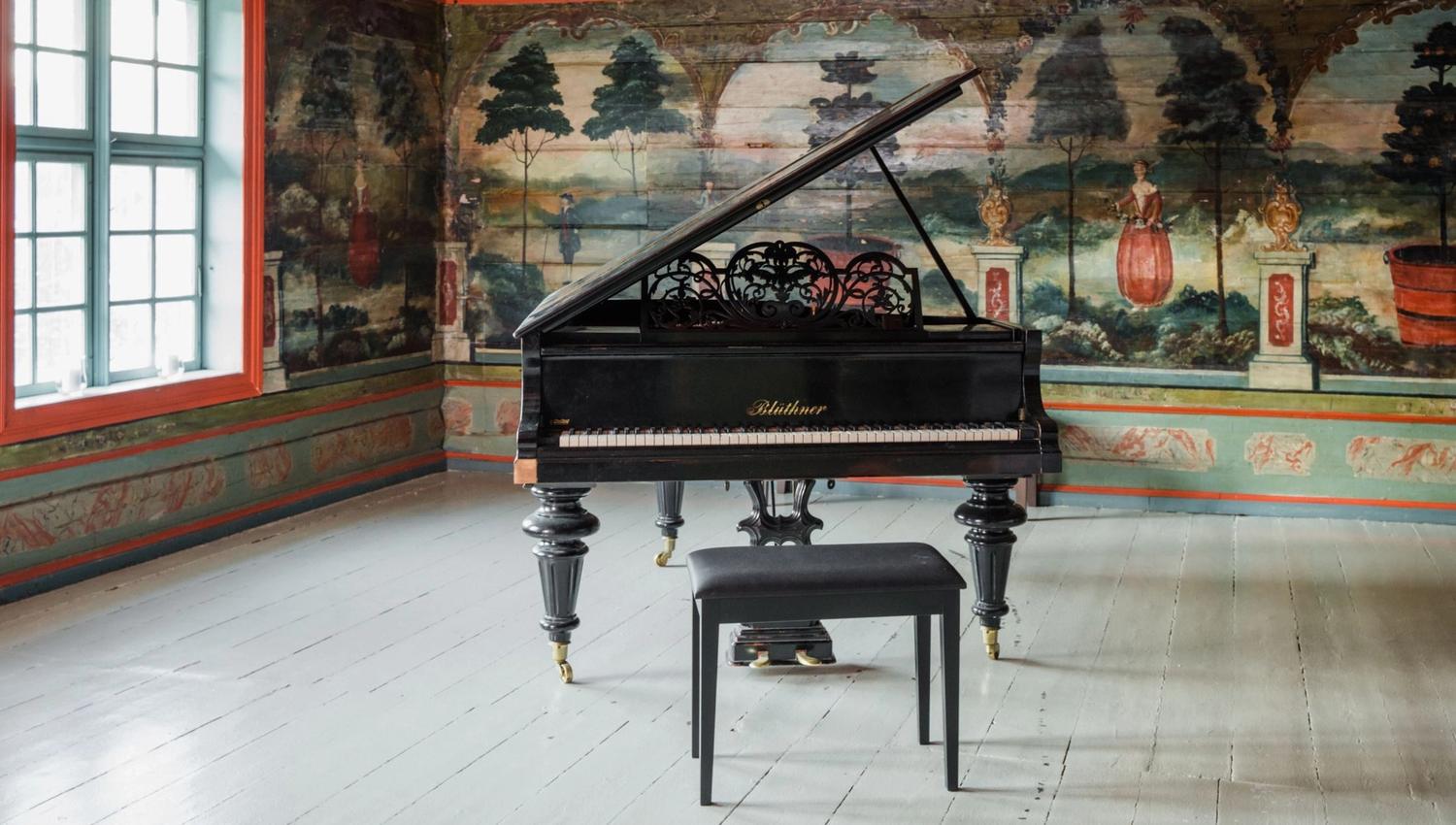 The Red Hall at Skrivergaarden, featuring a grand piano and decorative paintings on the original timber walls.