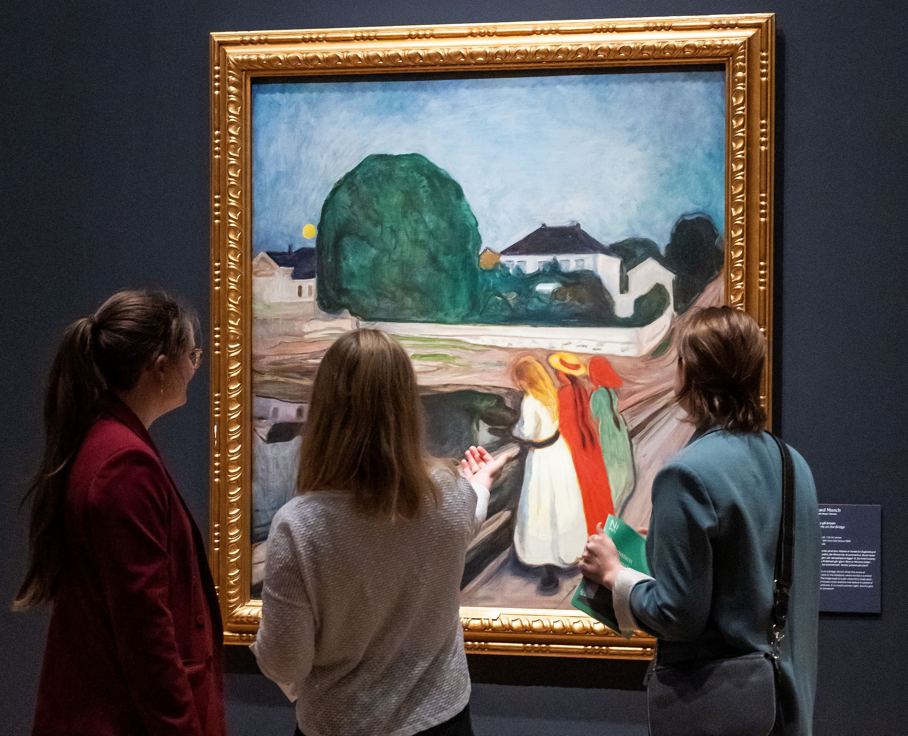 Three girls looking at the painting "Girls on a Bridge" by Edvard Munch.