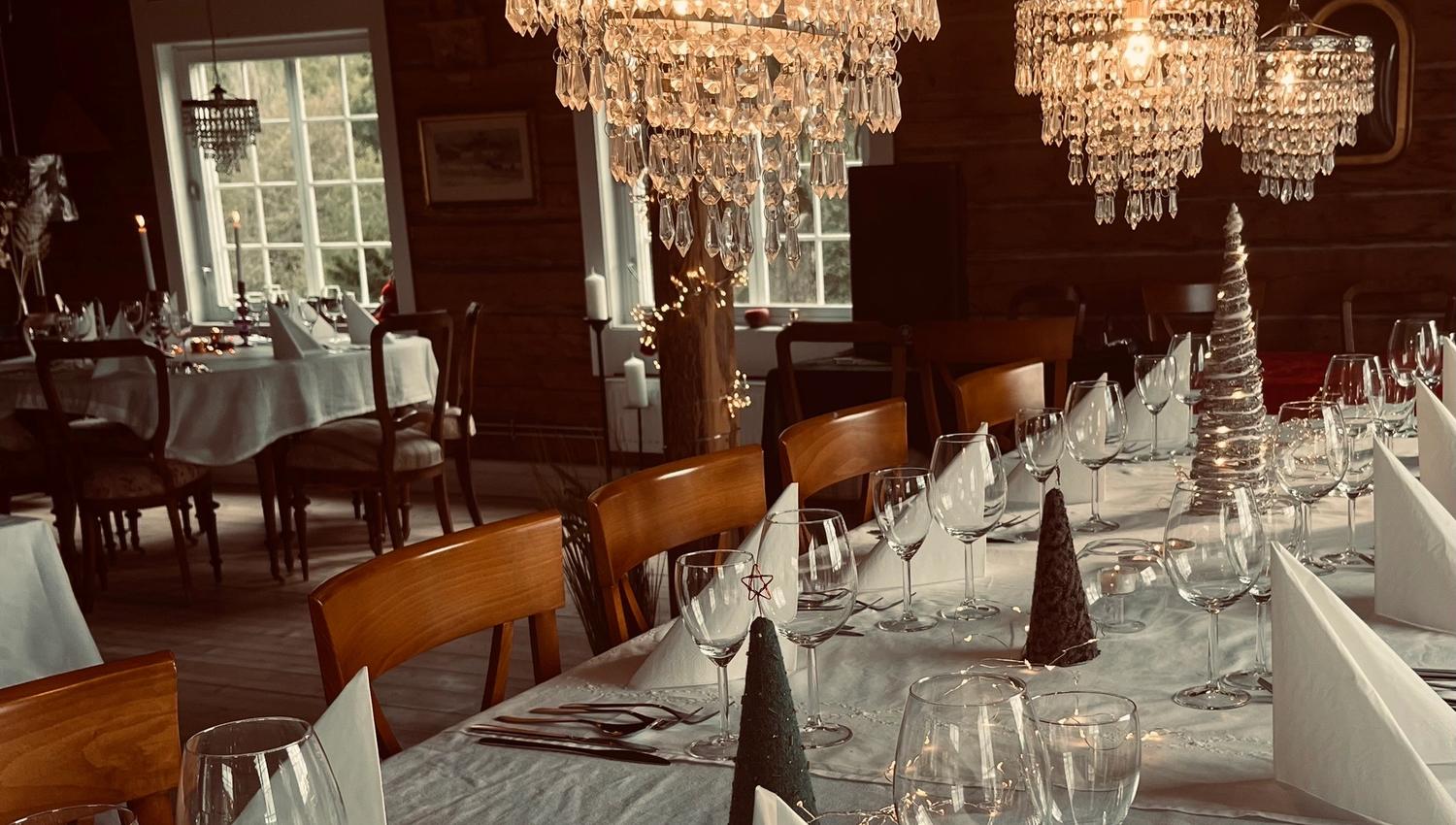 Elegant spisestue med trevegger, krystalllysekroner og bord dekket med hvite duker, servietter og glass.