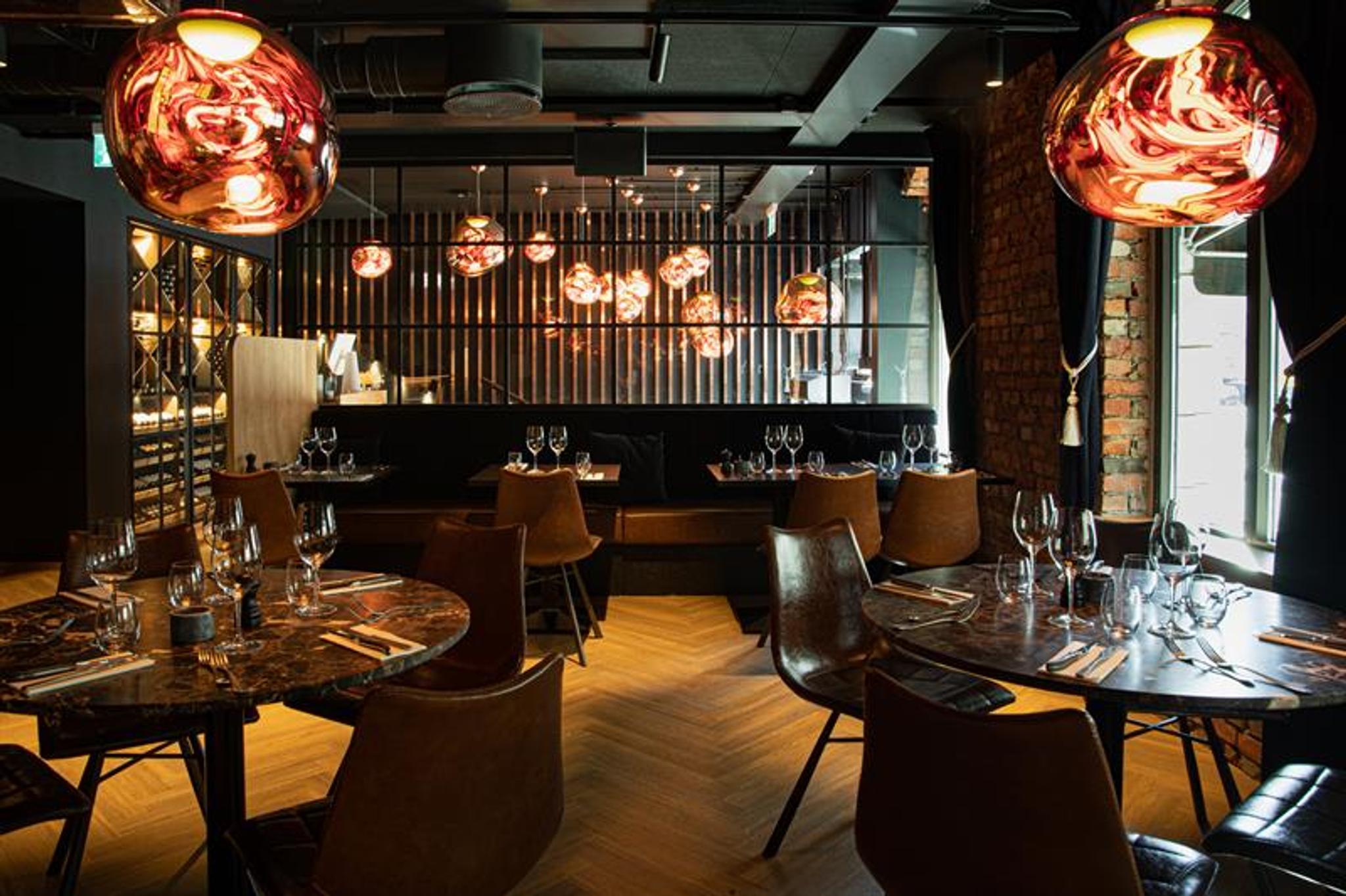 Restaurant interior with round, brown tables, brown chairs and seating section against the wall.