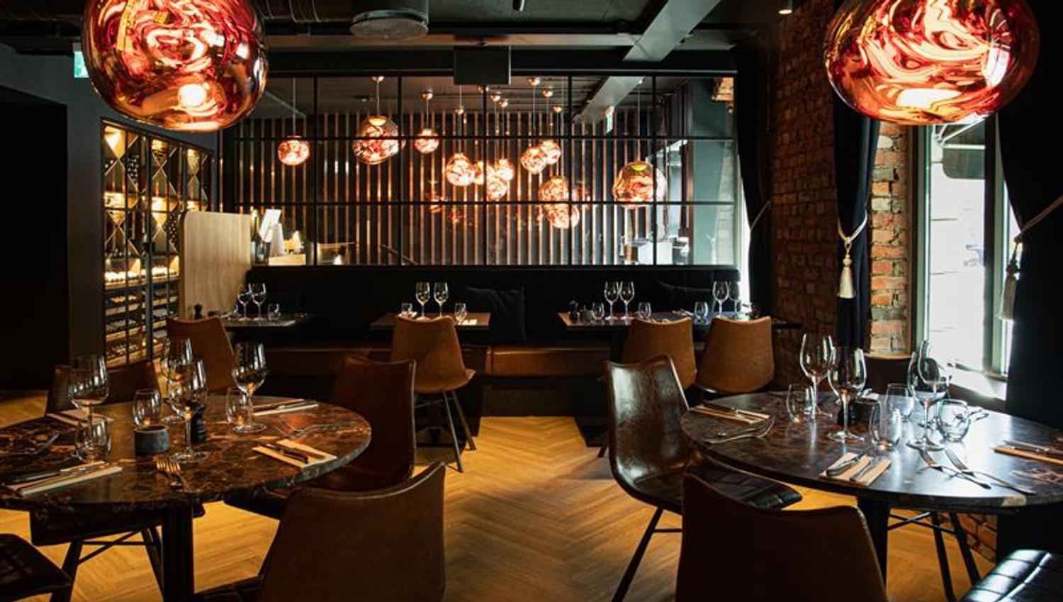 Restaurant interior with round, brown tables, brown chairs and seating section against the wall.