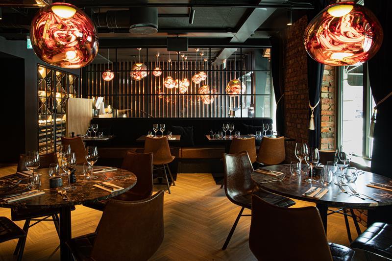 Restaurant interior with round, brown tables, brown chairs and seating section against the wall.