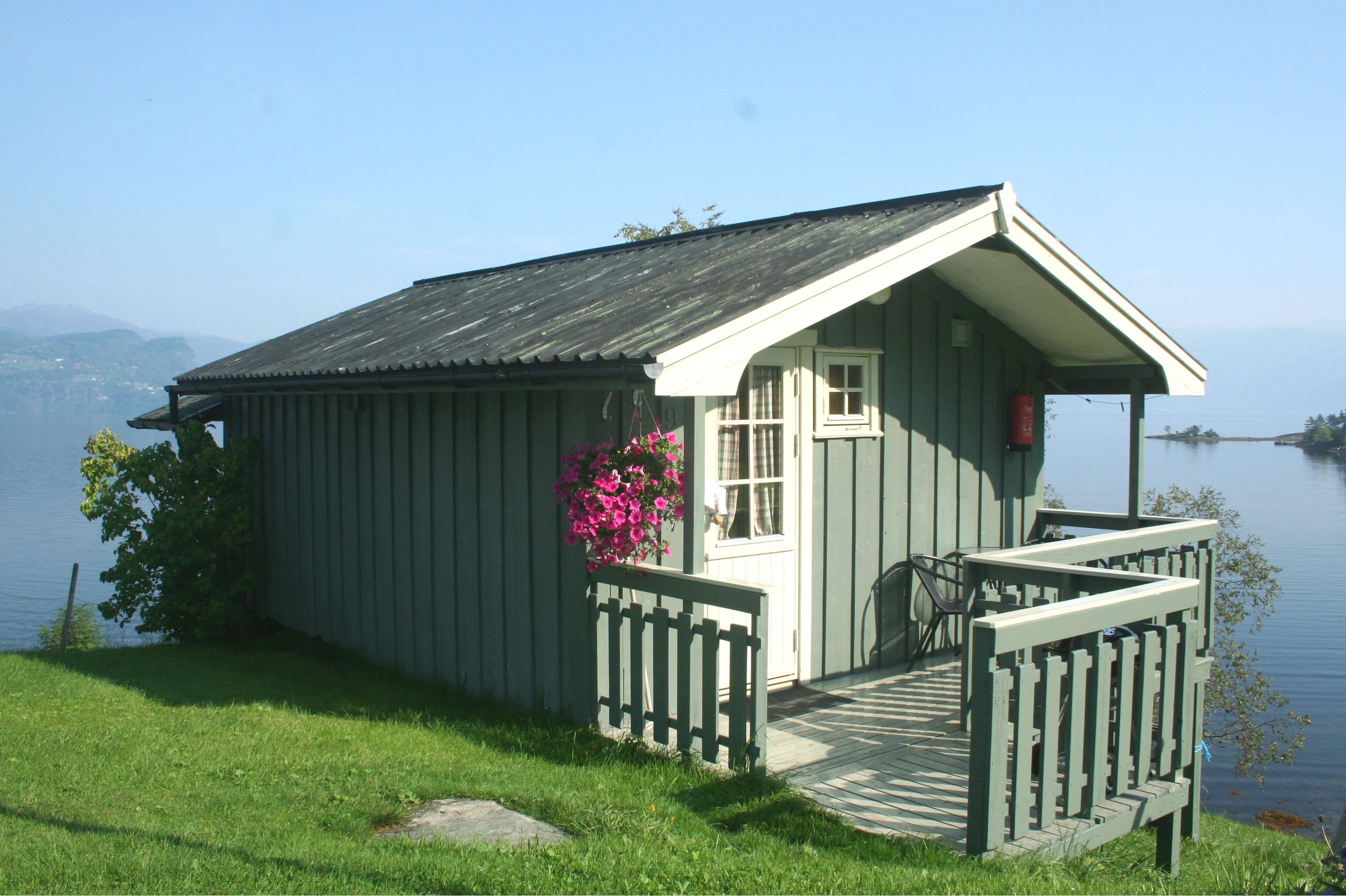 Small cabin with hanging flowers and a peaceful fjord view at Oddland Camping.