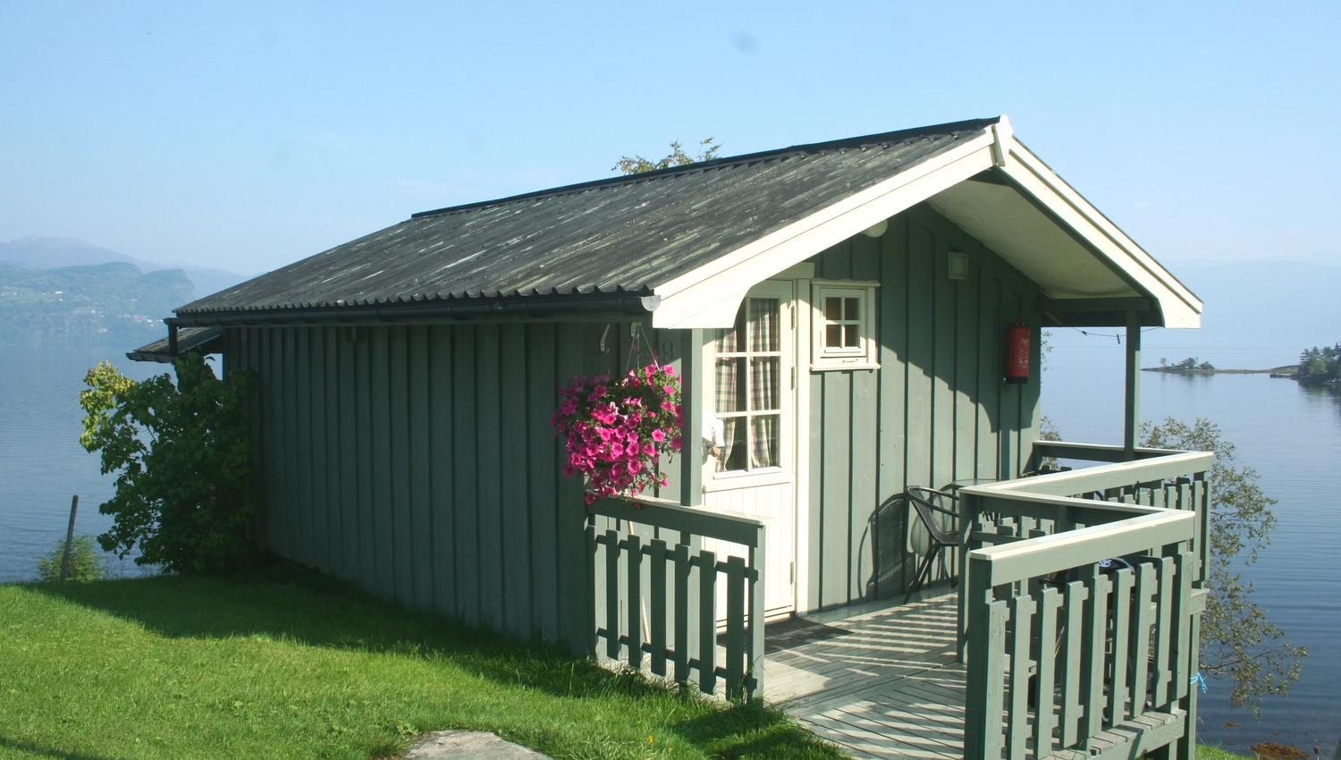 Small cabin with hanging flowers and a peaceful fjord view at Oddland Camping.