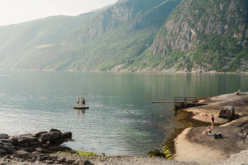 Kråkeskarvet beach with a person jumping from the diving board into the fjord. There are a lot of people sunbathing and swimming.