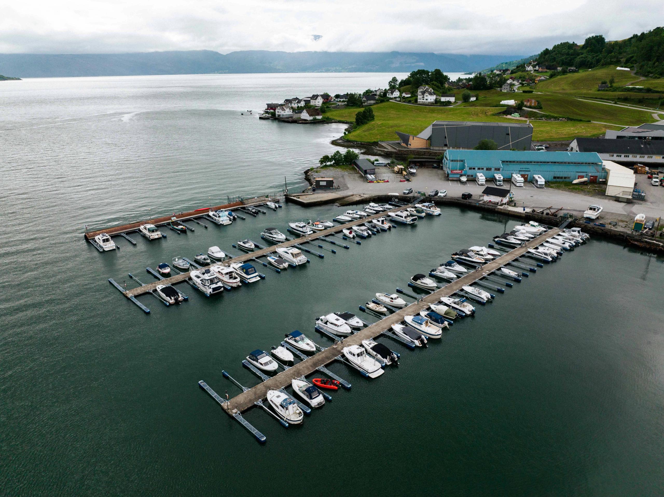 Aerial view of Øystese Guest Harbour in Hardanger, with boats moored along the floating docks and scenic fjord landscape in the background.