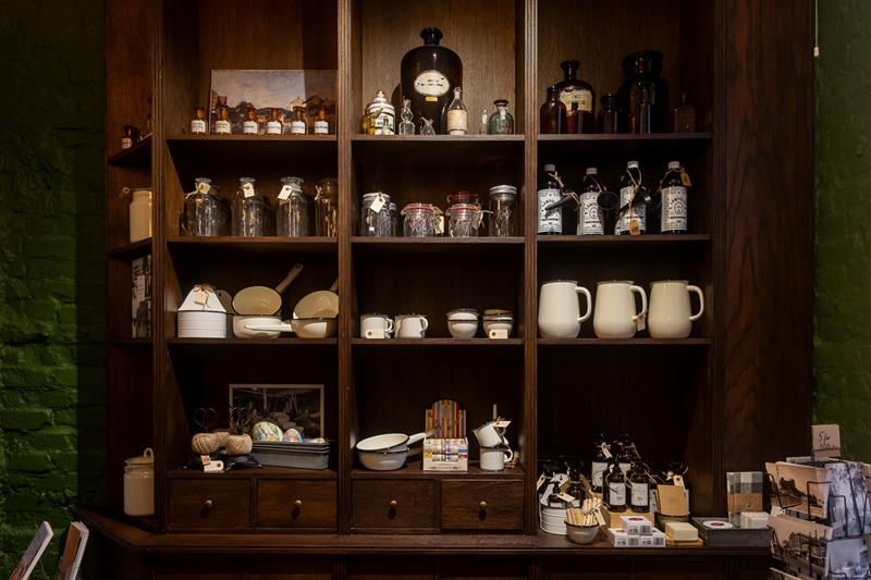 Museum display featuring shelves filled with glass jars, enamelware and historic household items.