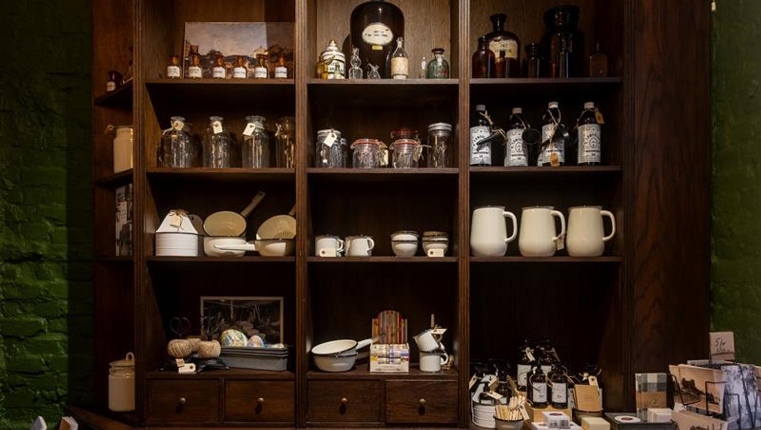 Museum display featuring shelves filled with glass jars, enamelware and historic household items.