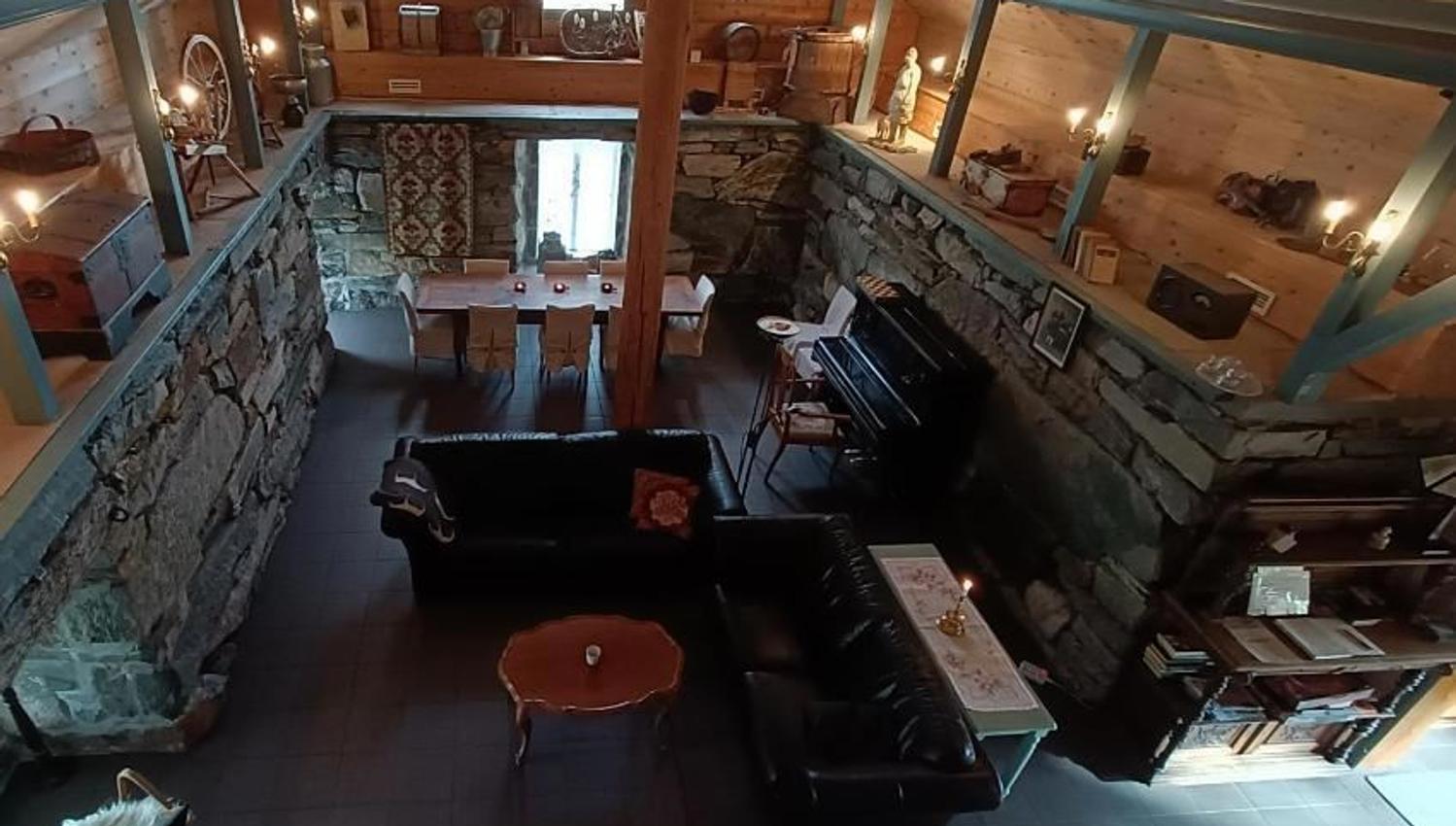 Orheimstunet in Nordfjord - View from a loft into a rustic room with stone walls, leather sofa, dining table, piano, and candlelight..