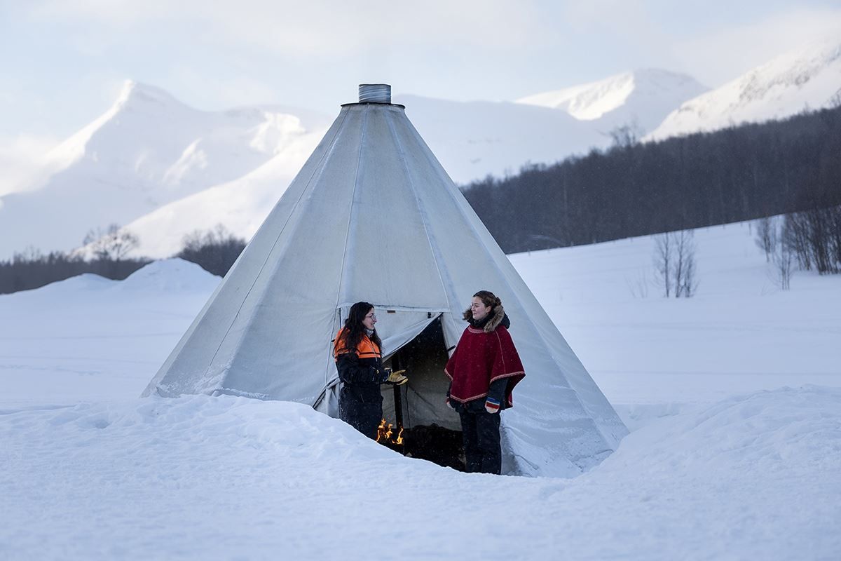Guests beside a traditional Sámi lavvu at Camp Tamok