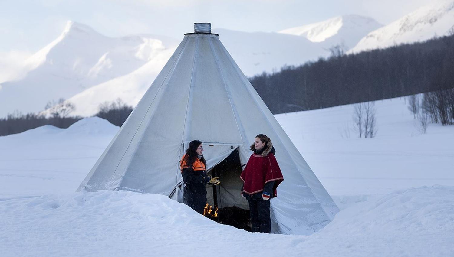 Guests beside a traditional Sámi lavvu at Camp Tamok
