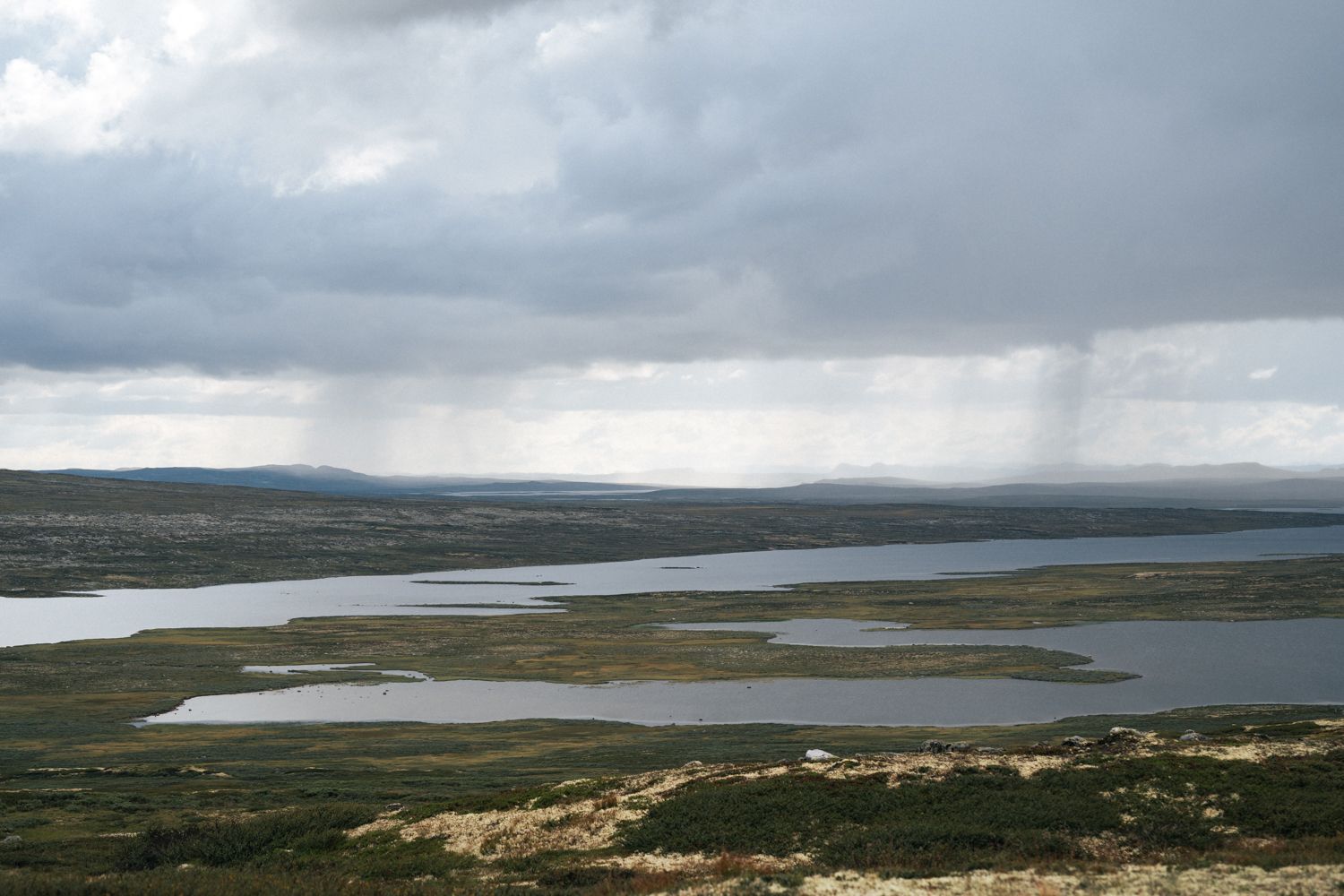 Viser et stort fjellvann under en overskyet himmel.