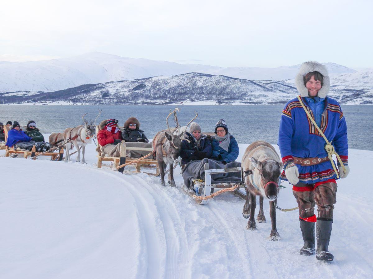 Guests travelling by reindeer sled through a snowy winter landscape with a guide from Tromsø Arctic Reindeer.