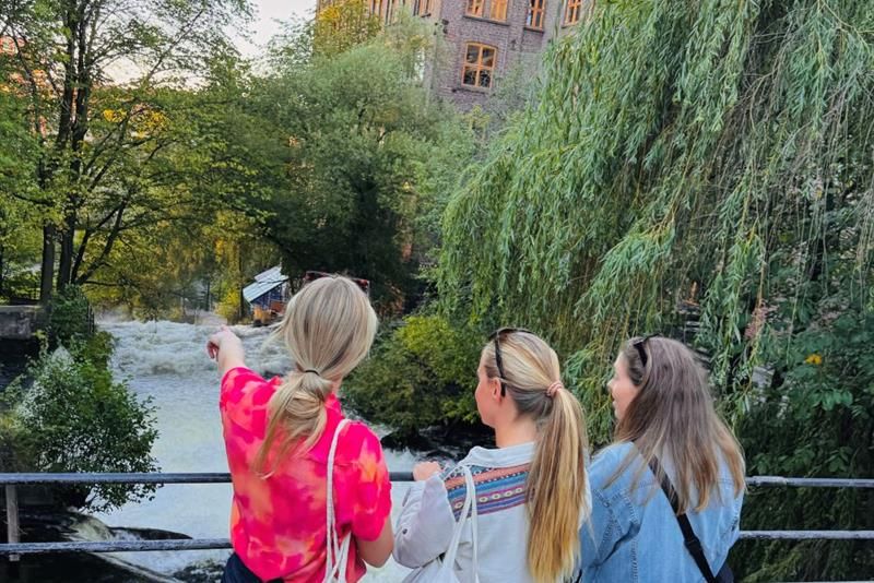 Three girls standing on a bridge watching over the Akerselva river
