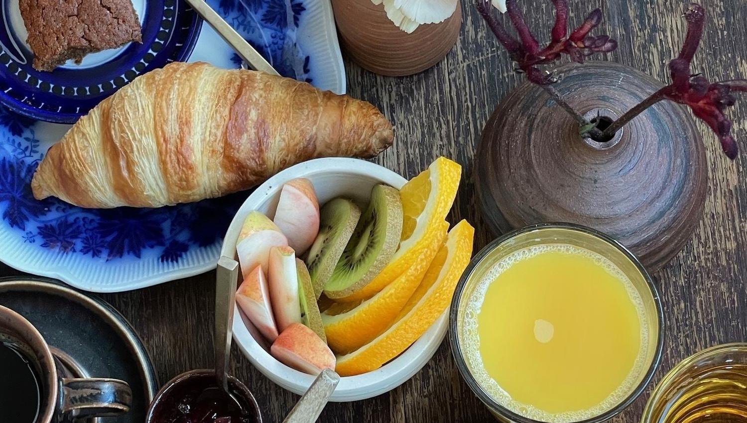 Frokostbord med croissant, kake, granola, frukt, juice og te