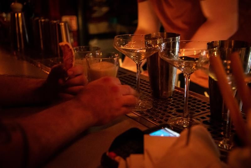 Nærbilde av diverse hender og drinker på en bardisk.