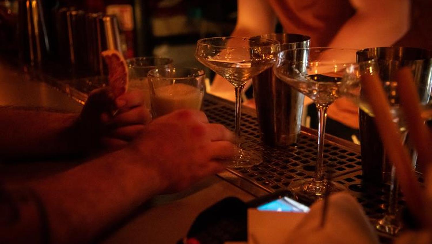 Nærbilde av diverse hender og drinker på en bardisk.