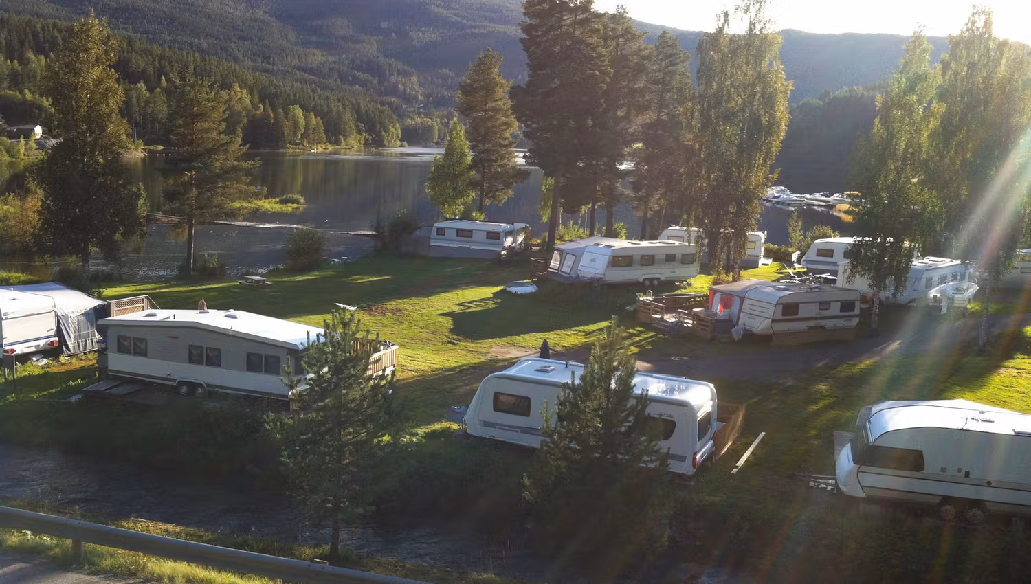 A campground by a lake during summer with caravans on a green lawn.