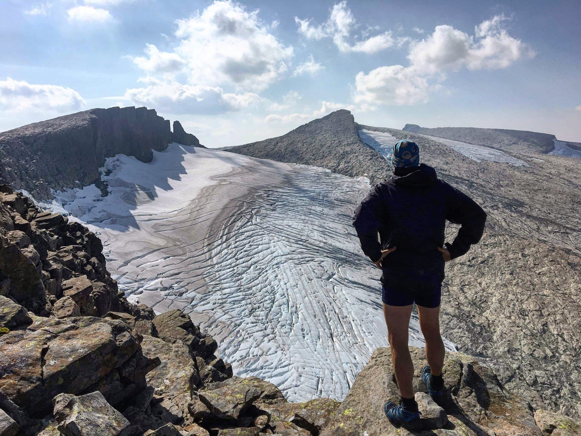 Opplevingar i nærleiken av Bremanger Fjordhotell: Ein turgåar står på ein steinrygg og ser utover Ålfotbreen mellom steinete fjell under blå himmel..