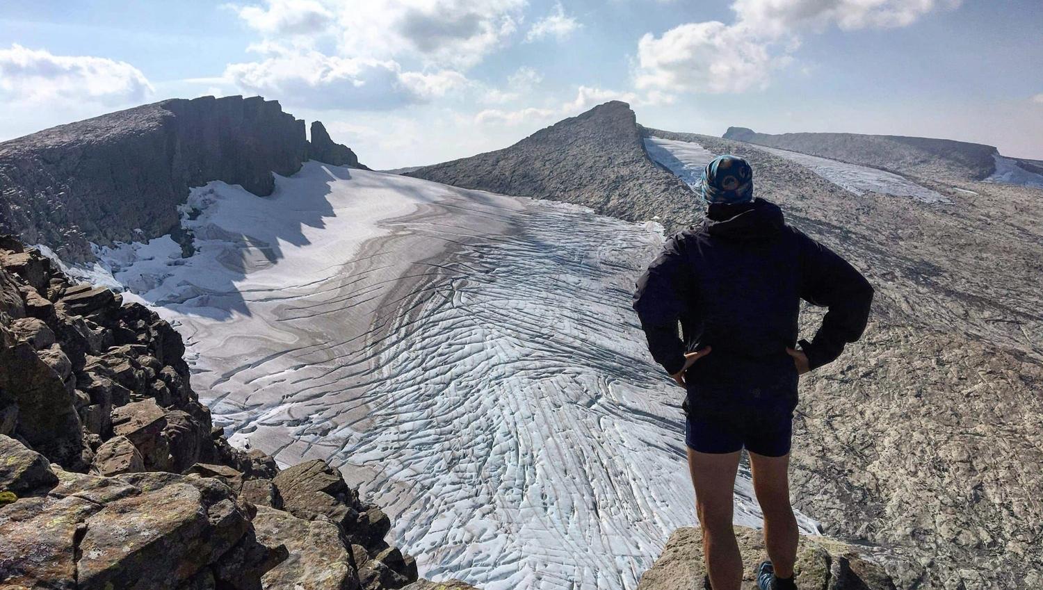 Opplevingar i nærleiken av Bremanger Fjordhotell: Ein turgåar står på ein steinrygg og ser utover Ålfotbreen mellom steinete fjell under blå himmel..