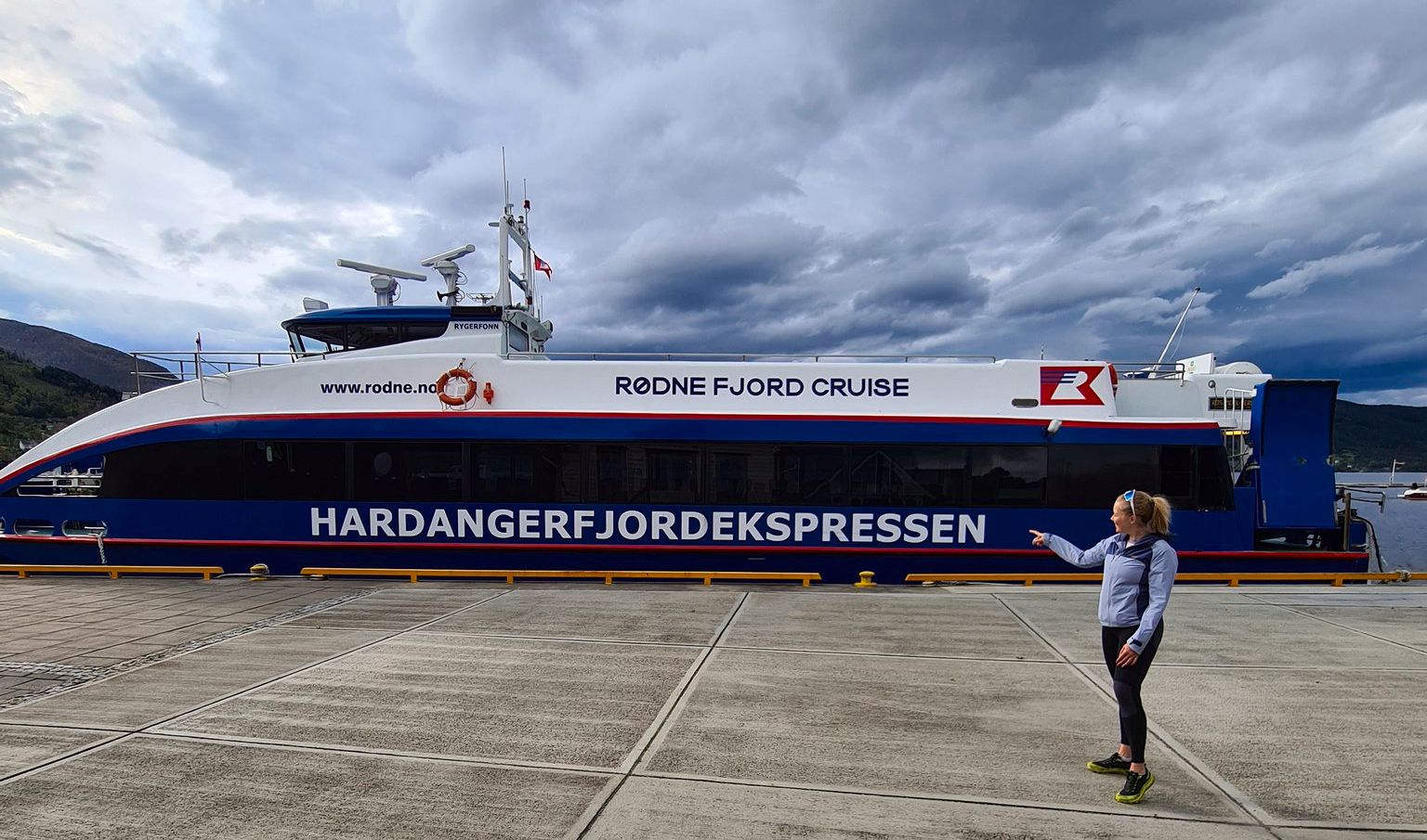 Hardangerfjordekspressen at the dock, with a traveler pointing towards the boat and fjord view.
