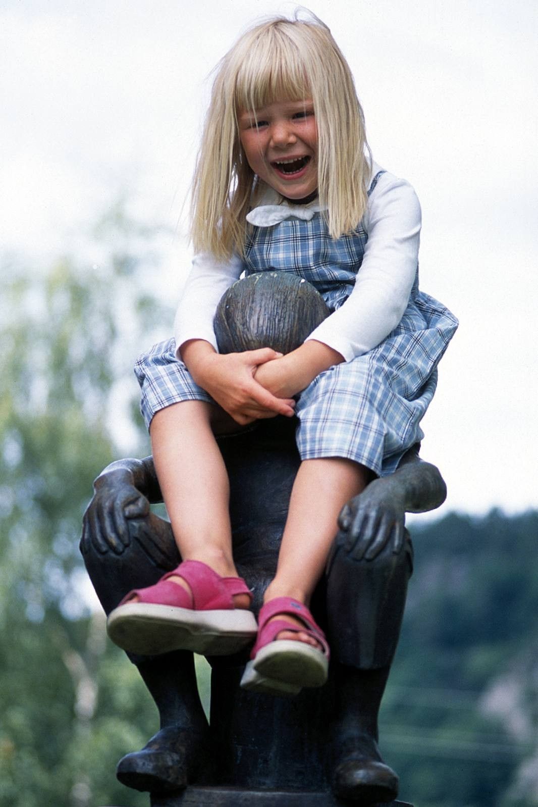 Smilende jente som sitter på en skulptur