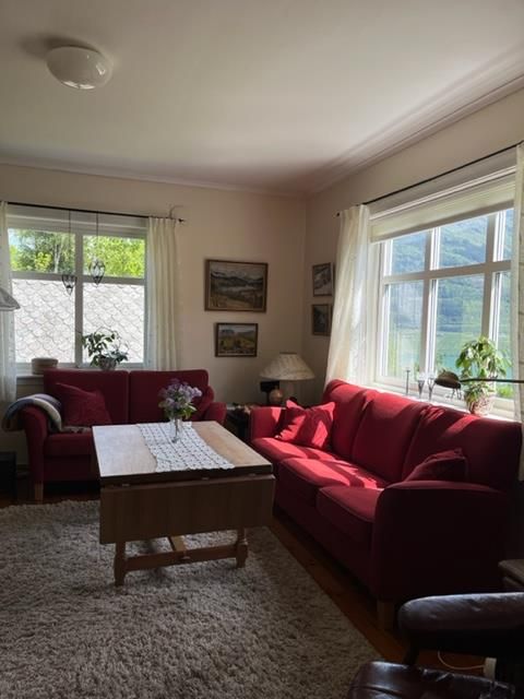 Bright and inviting living room at Jaastad Gjestetun featuring red sofas, natural décor, and views of the Hardanger scenery.