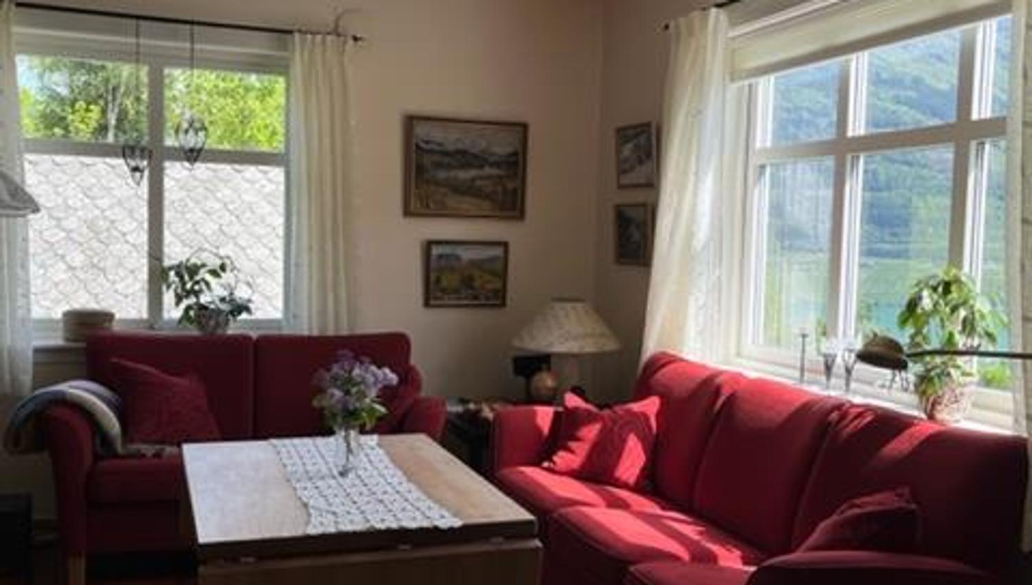 Bright and inviting living room at Jaastad Gjestetun featuring red sofas, natural décor, and views of the Hardanger scenery.
