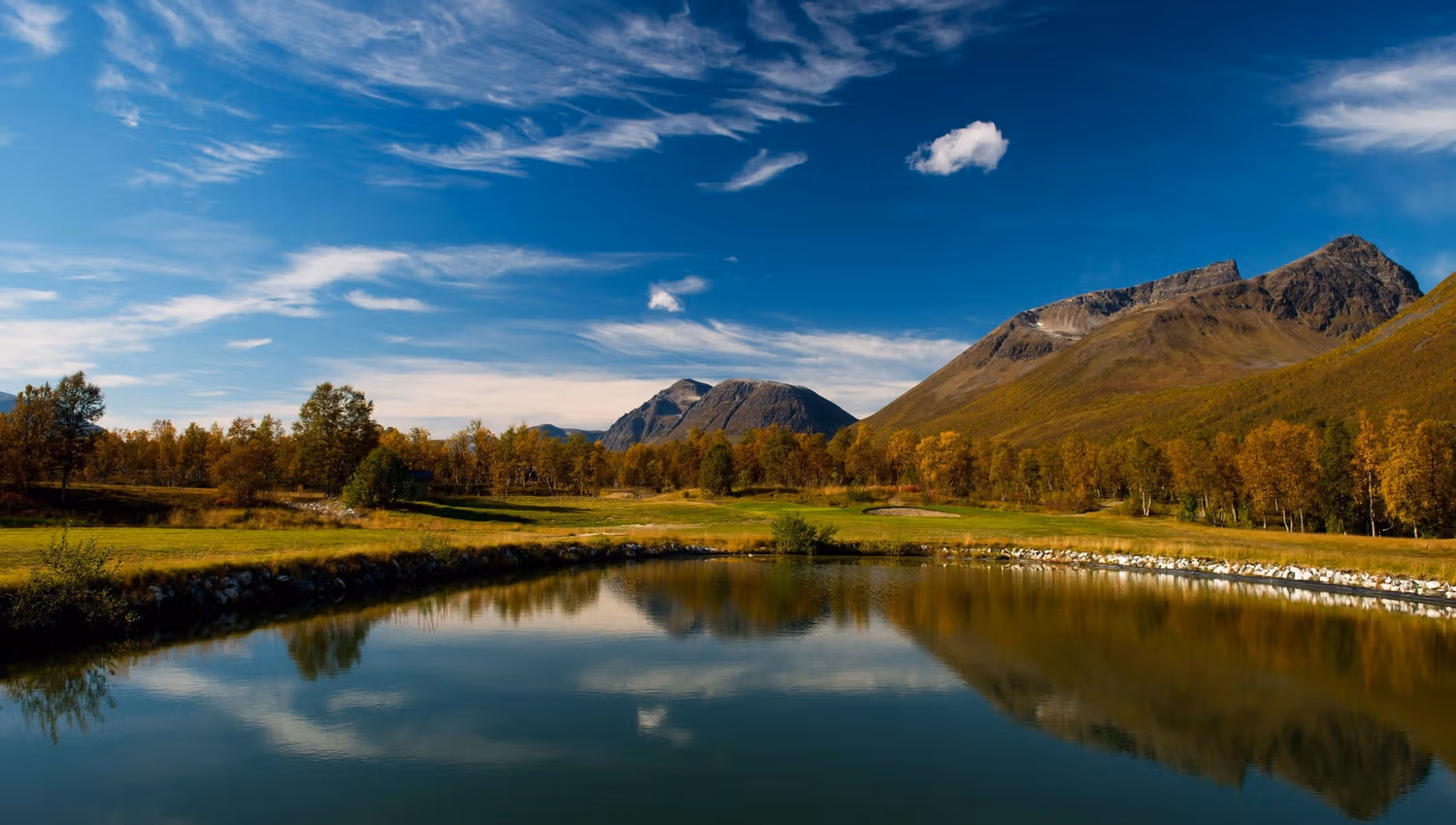Mountain landscape with a lake, autumn-coloured trees, and a clear sky.