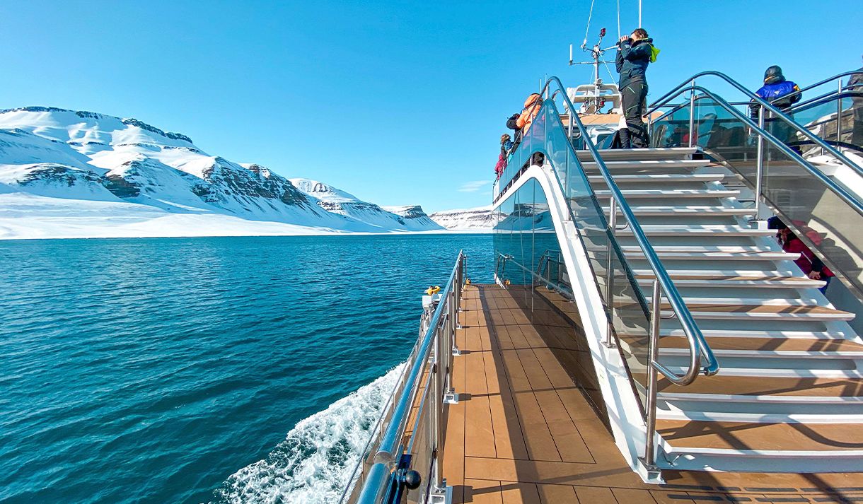 A boat sailing through a fjord with guests on board and snow-covered mountains in the background