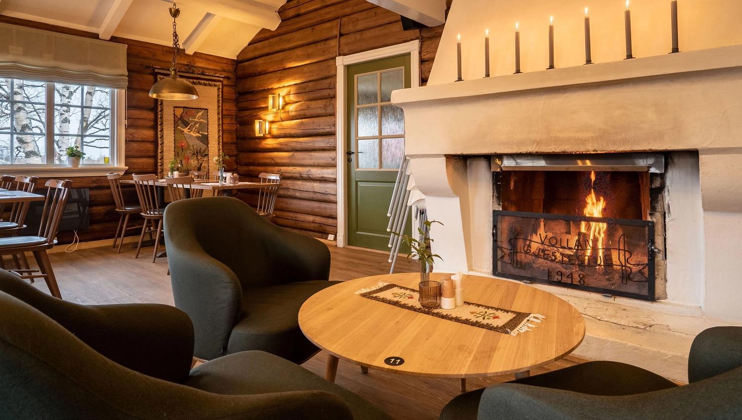 Rustic living room with fireplace, armchairs, and dining area by large windows