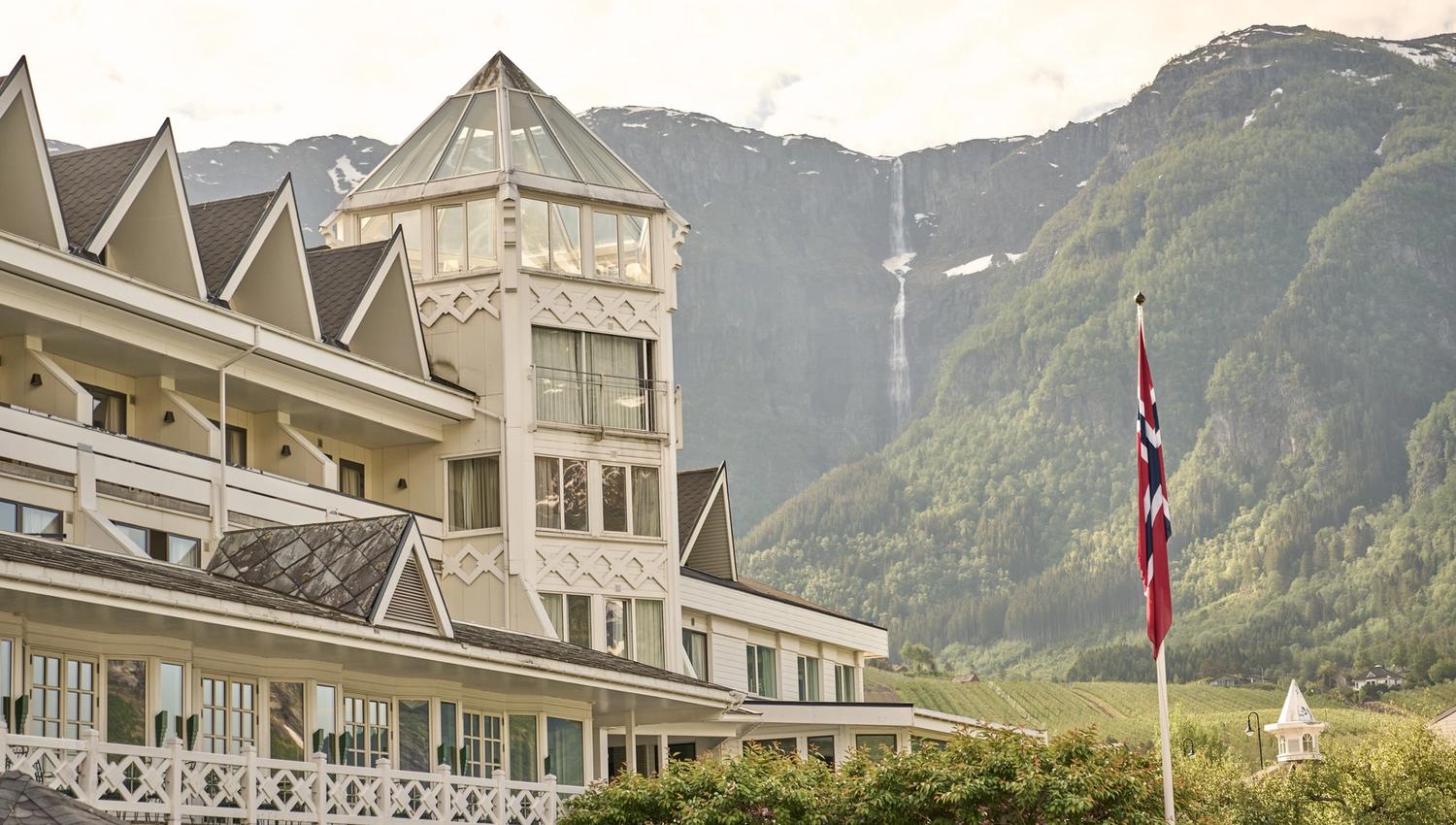 The iconic tower of Hotel Ullensvang with a dramatic waterfall cascading down the mountainside.