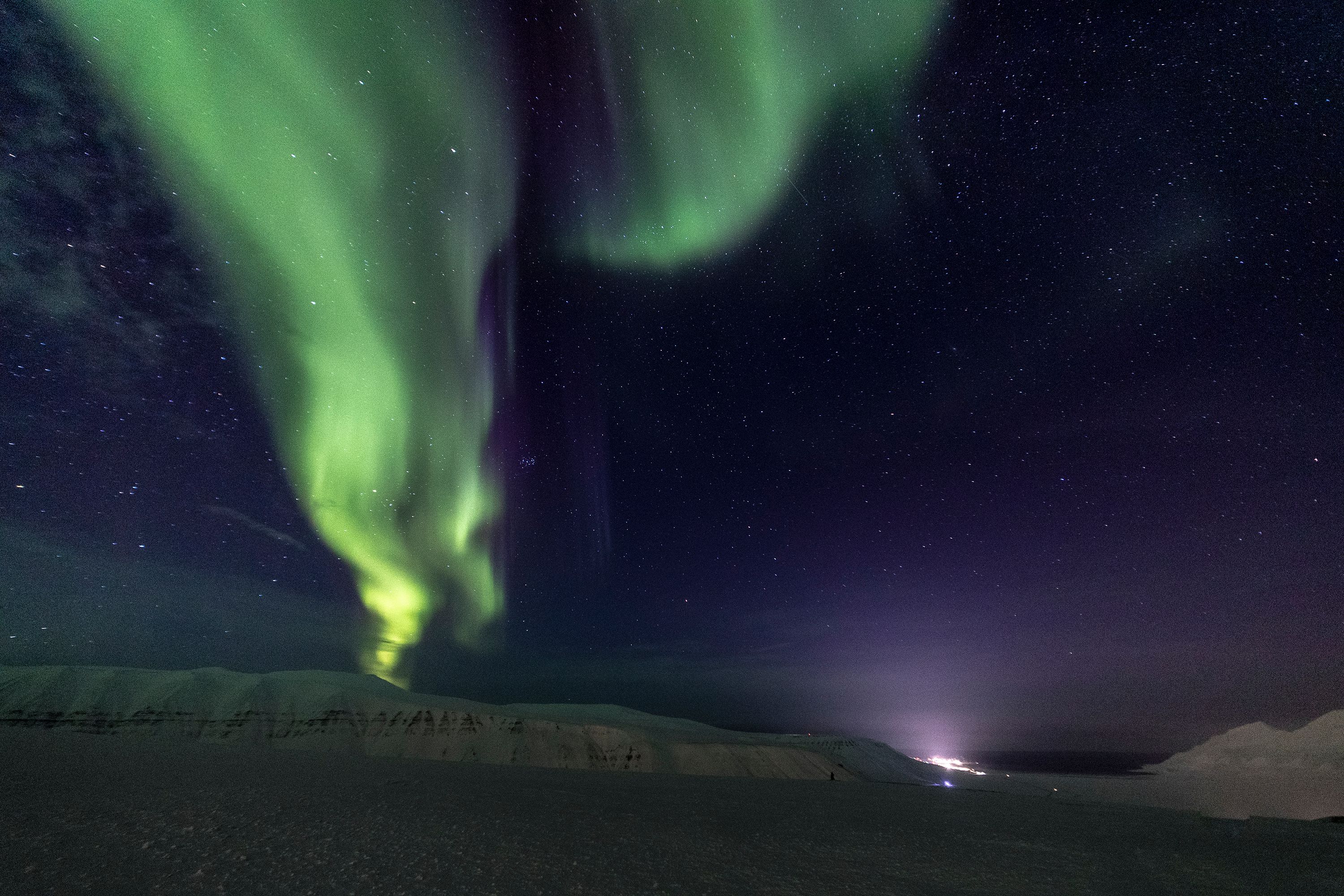 A stripe of green northern lights dancing above the snowcovered mountains 